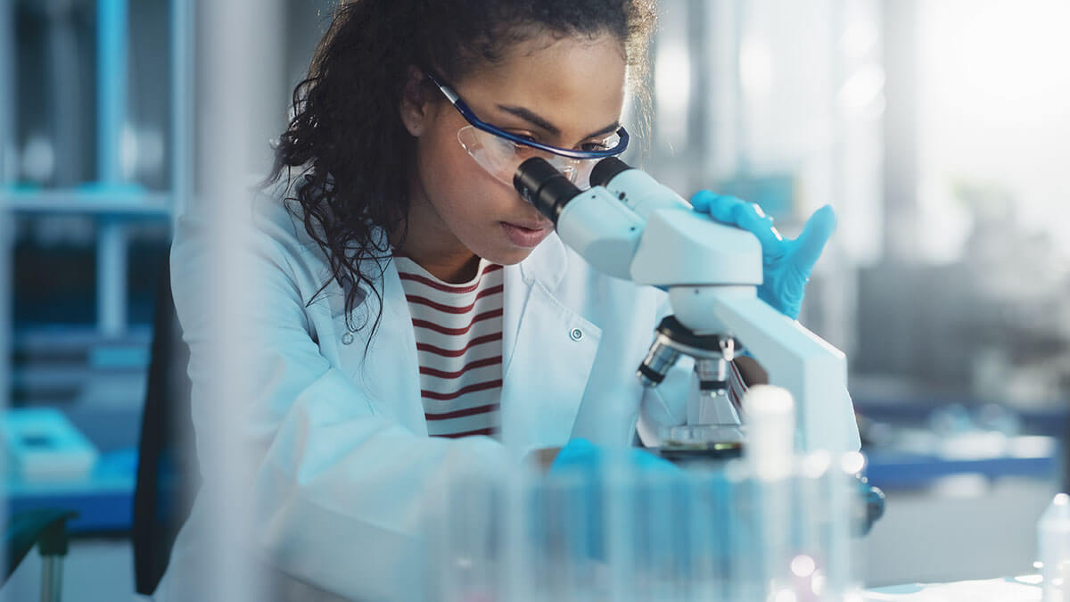 Portrait of a female scientist looking under a microscope analysing a test sample.