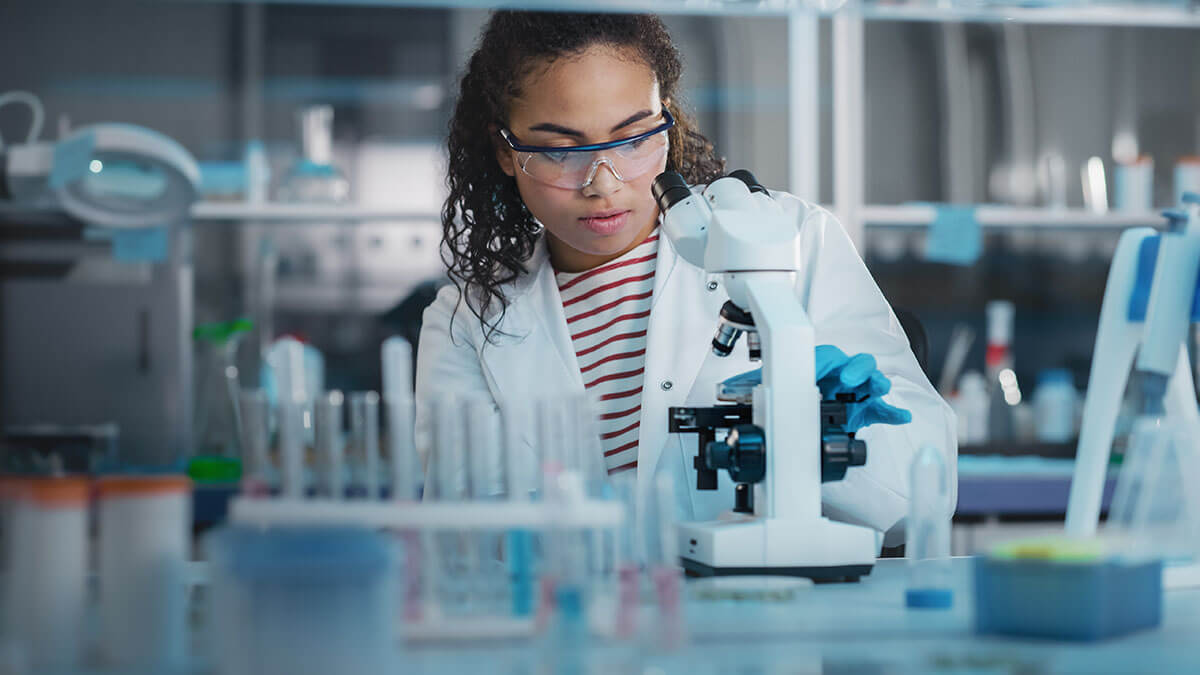 Portrait of a female scientist looking under a microscope analysing a test sample.